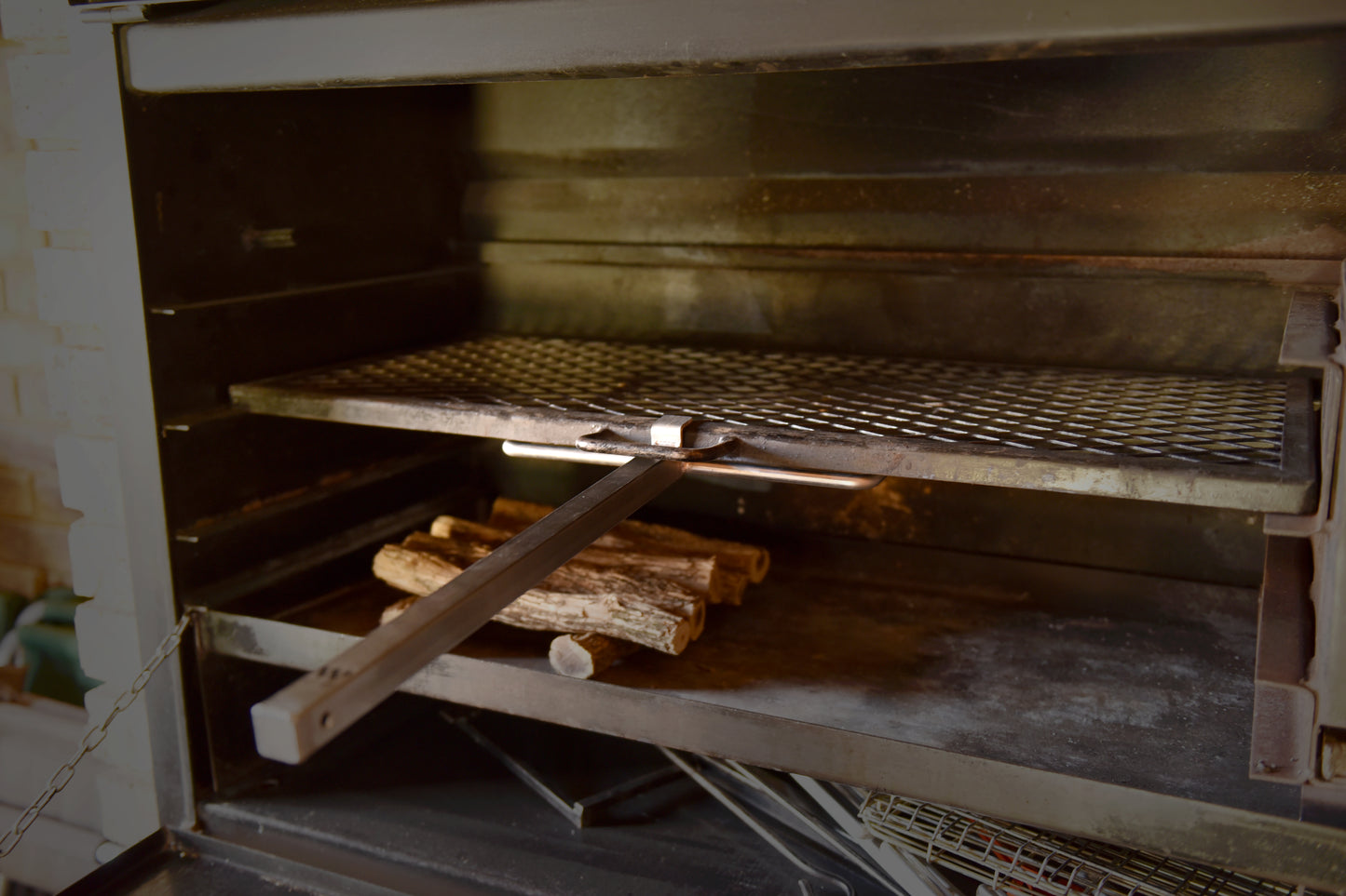 A steel braailift inside a braai setup, positioned over a small stack of wood, with a long handle extending outwards.