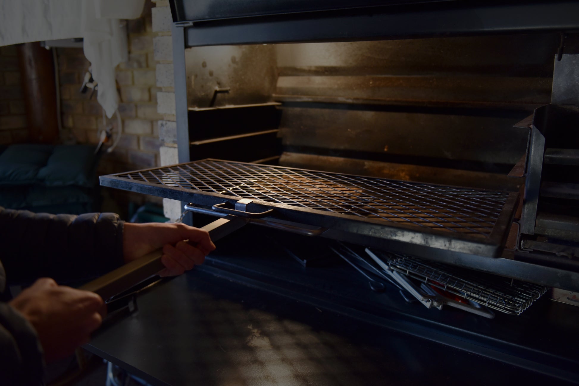 Person holding a braailift attached to a braai grid, pulling the grid out of a built in braai