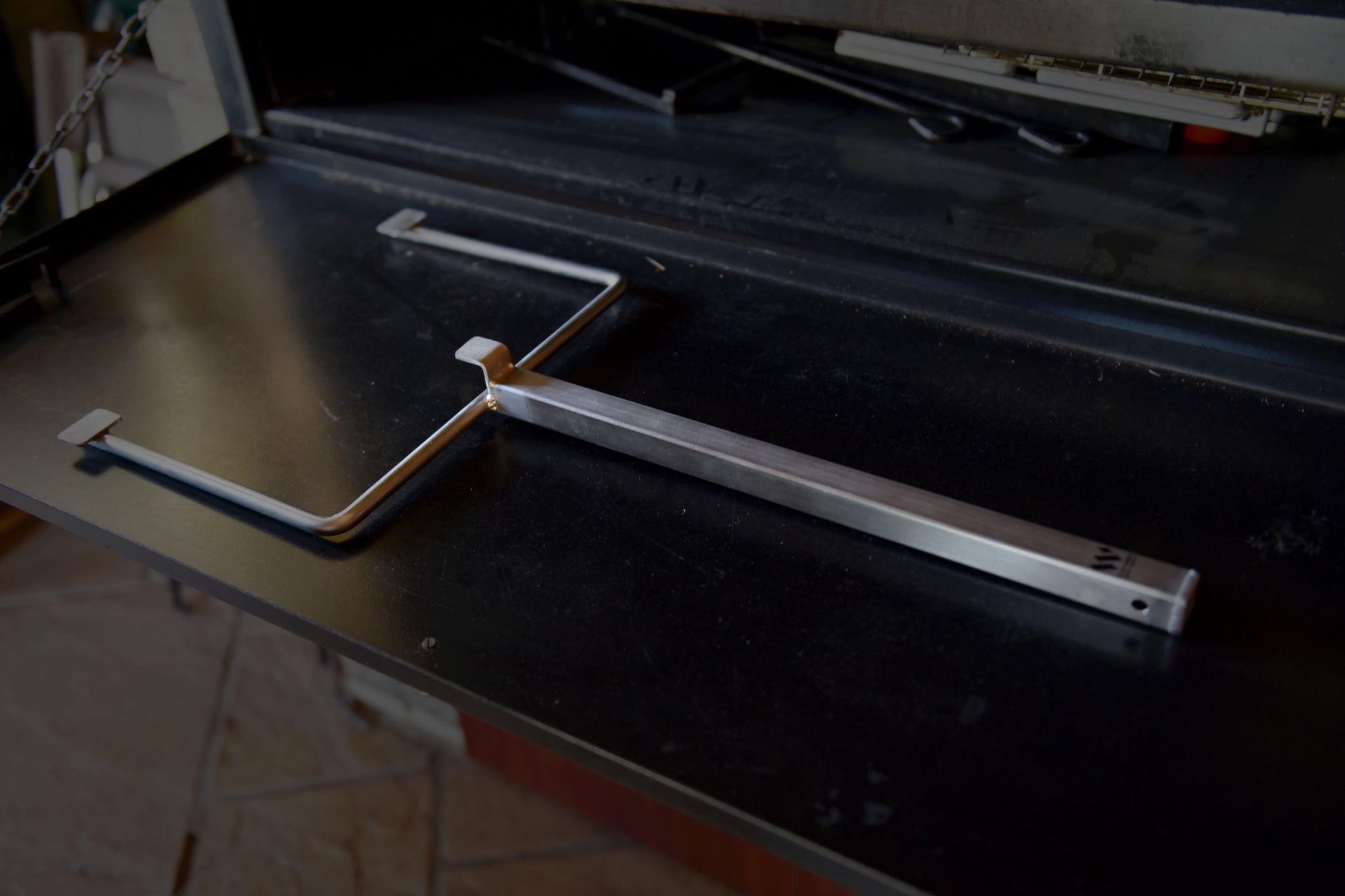 The Braai Lift’s specialized lifting tool placed on a black surface, highlighting its design for easy and safe grid manipulation during braai sessions.