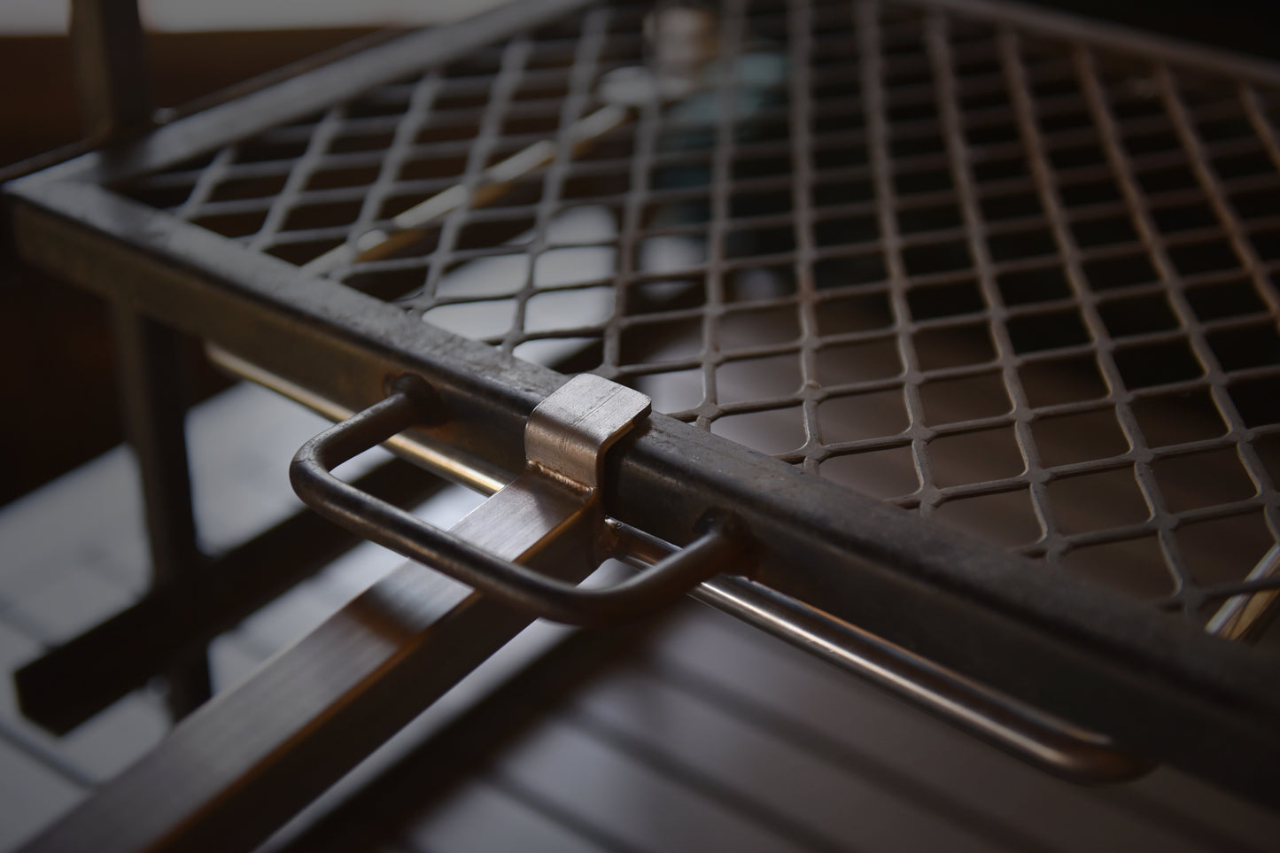 Close-up view of the Braai Lift’s steel grilling grate and locking mechanism, highlighting the robust construction and easy-to-use handle attachment.