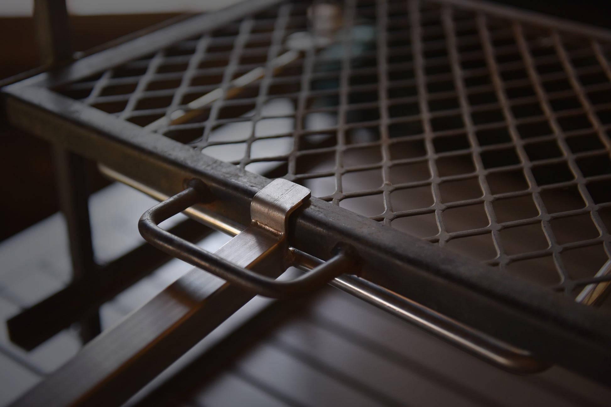 Close-up view of the Braai Lift’s steel grilling grate and locking mechanism, highlighting the robust construction and easy-to-use handle attachment.