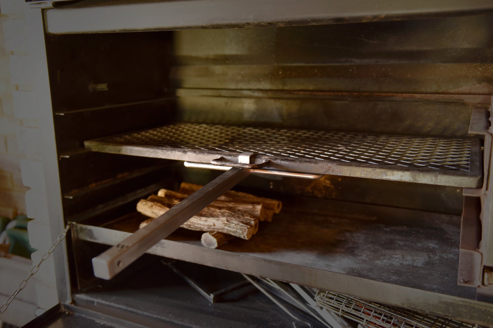 A steel braailift inside a braai setup, positioned over a small stack of wood, with a long handle extending outwards.