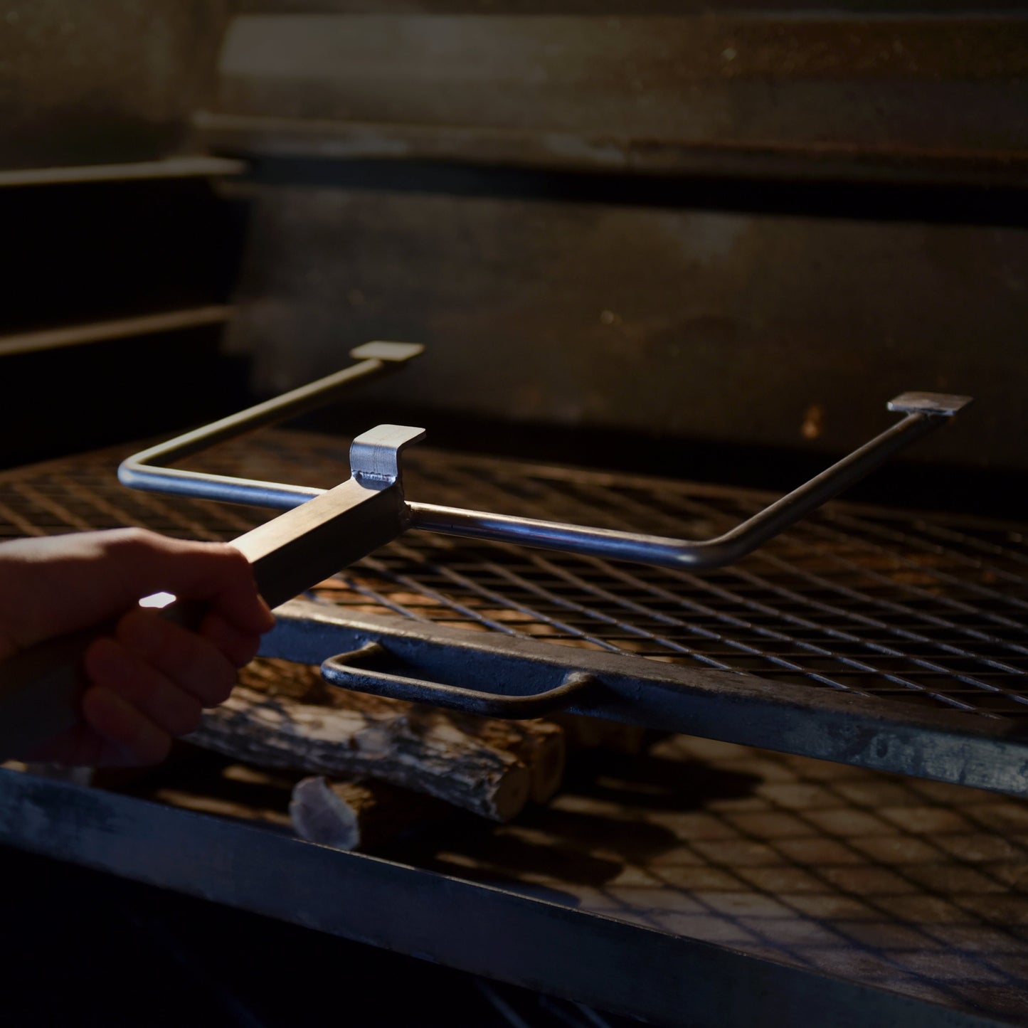 Person using a braailift to adjust the position of a steel grilling grate within a built in braai.