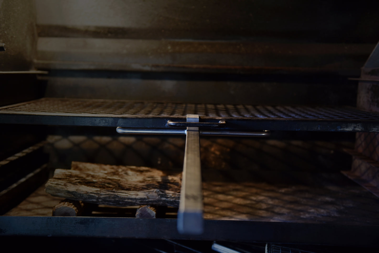 Front view of a braailift in action in a built in braai, with a handle and metal latch mechanism aligned in the center.