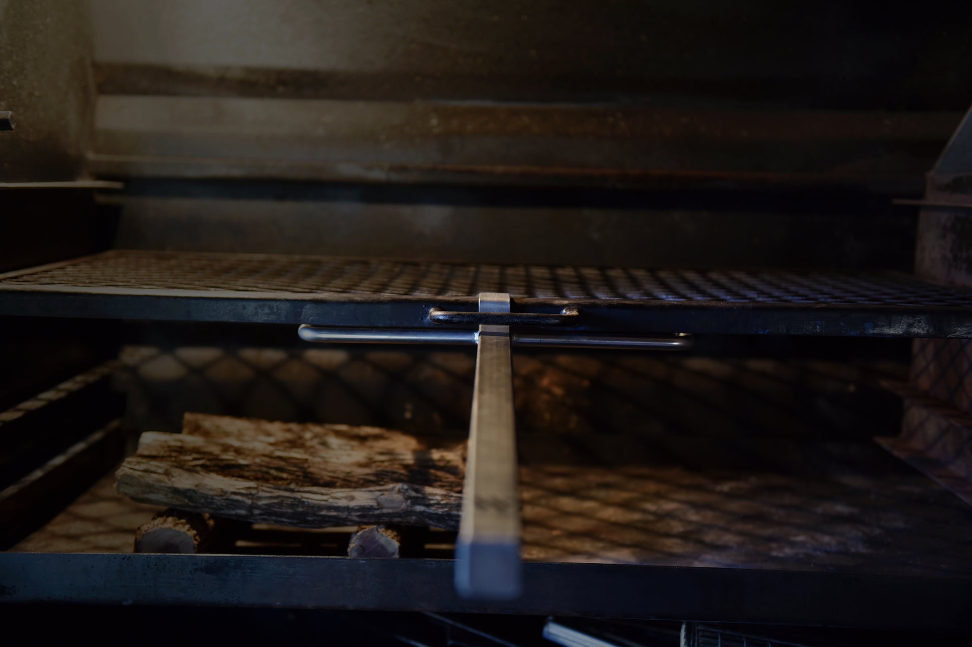 Front view of a braailift in action in a built in braai, with a handle and metal latch mechanism aligned in the center.